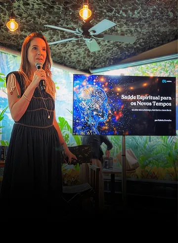 Fabíola Carvalho ao microfone em uma experiência, diante de um telão