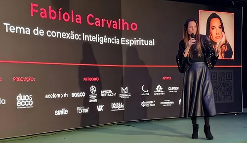Fabíola Carvalho palestrando no palco, diante de um telão com o tema da palestra