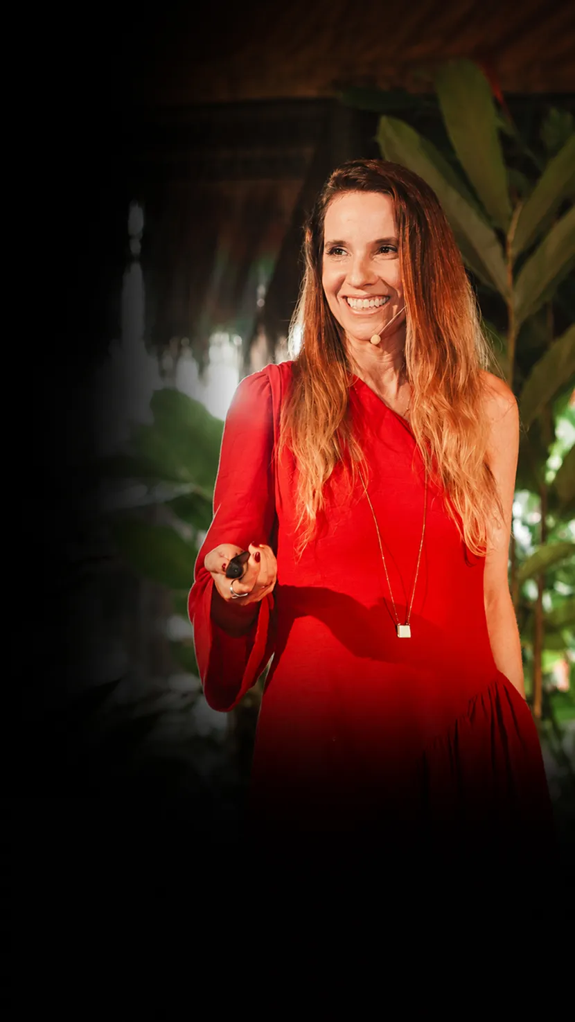 Fabíola Carvalho sorrindo no palco, de vestido vermelho, entre a vegetação
